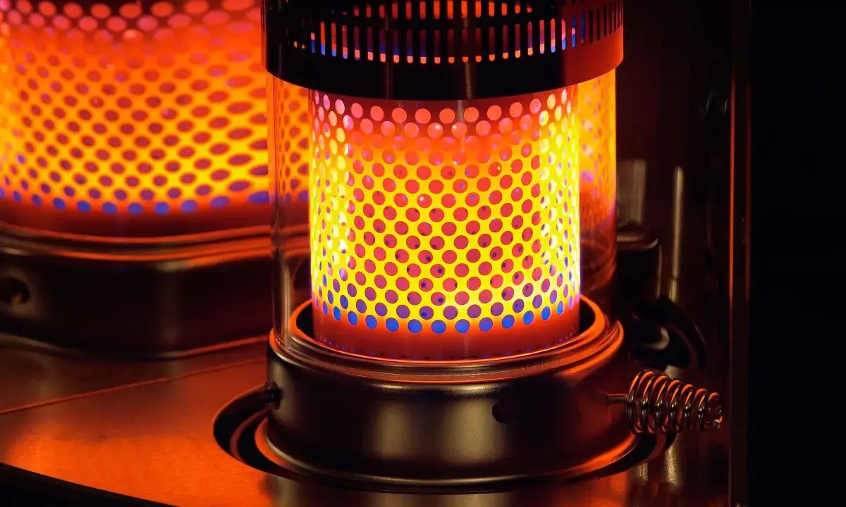 Estufa de parafina encendida, con llama naranja y azul visible a través de perforaciones. Pros y contras de su uso.