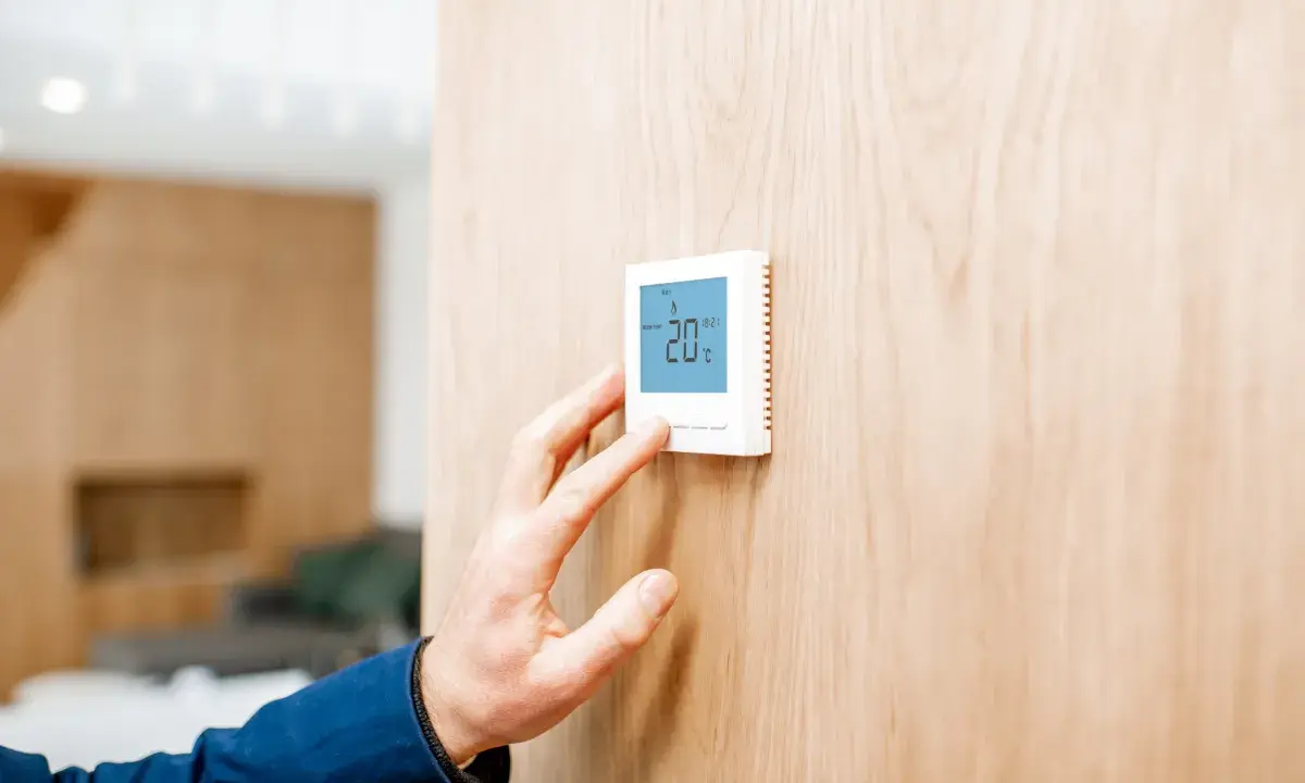 Mano ajustando un termostato digital, parte de los sistemas de calefacción, mostrando 20°C en una pared de madera.