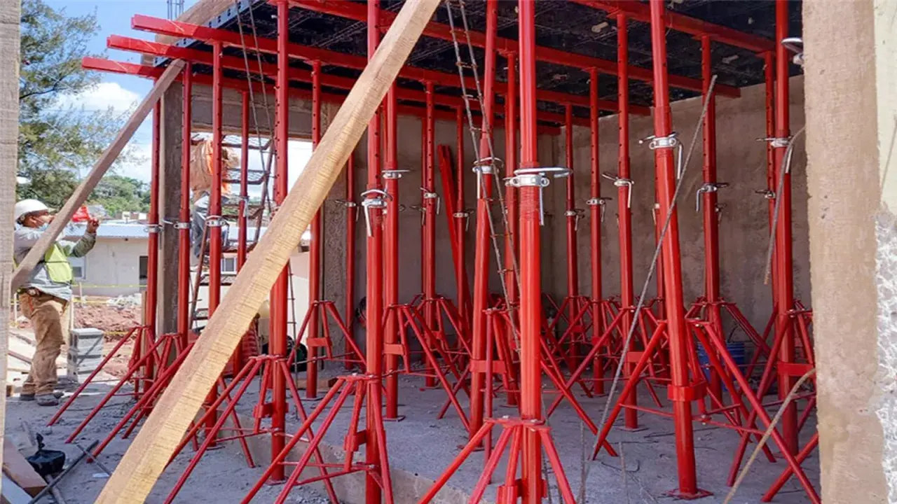 Construcción con varios tipos de puntales rojos sosteniendo una estructura. Un trabajador supervisa.
