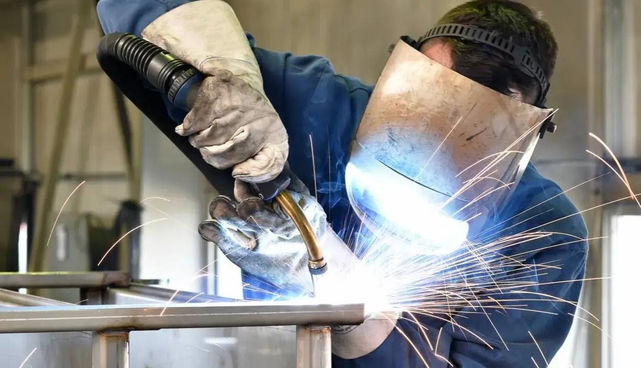 Soldador con máscara y guantes, demostrando cómo soldar con electrodo, creando chispas brillantes.