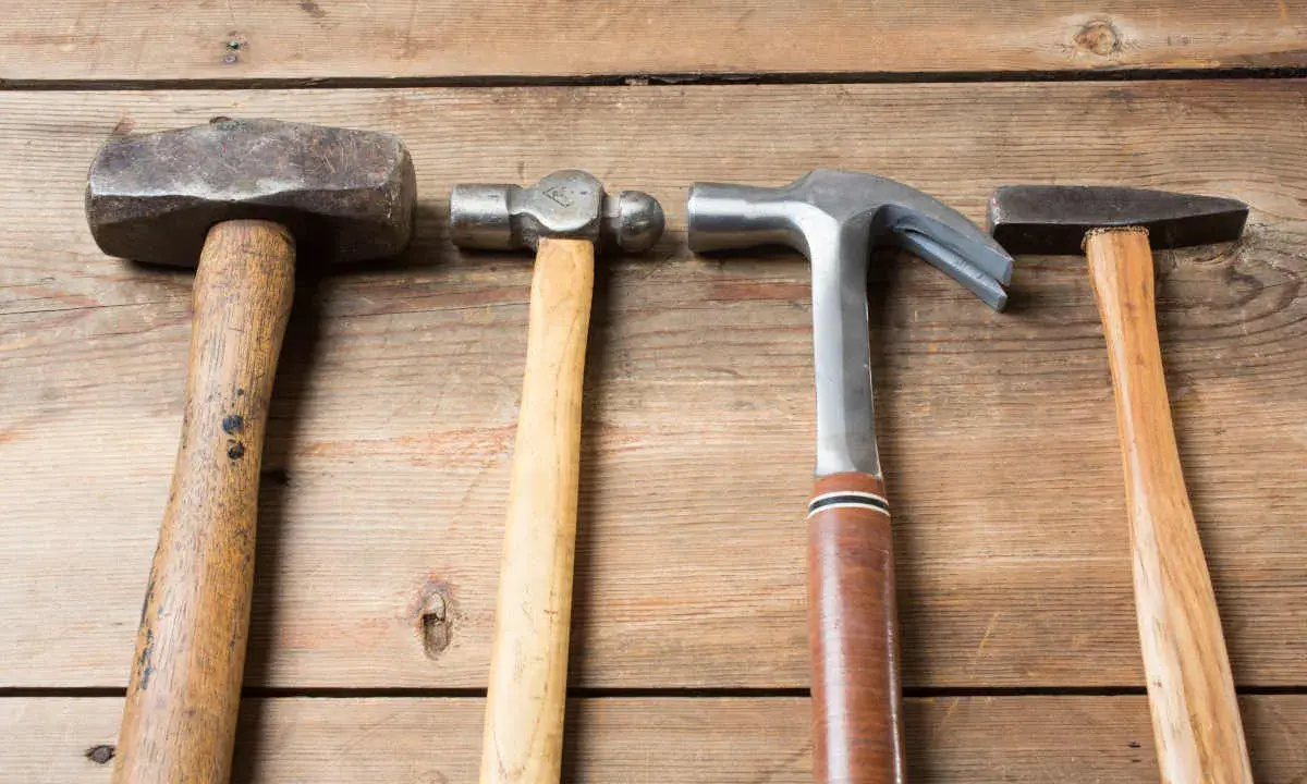 Cuatro martillos de diferentes clases: uno de orejas, uno de bola, uno de carpintero y uno de ebanista, sobre una superficie de madera.