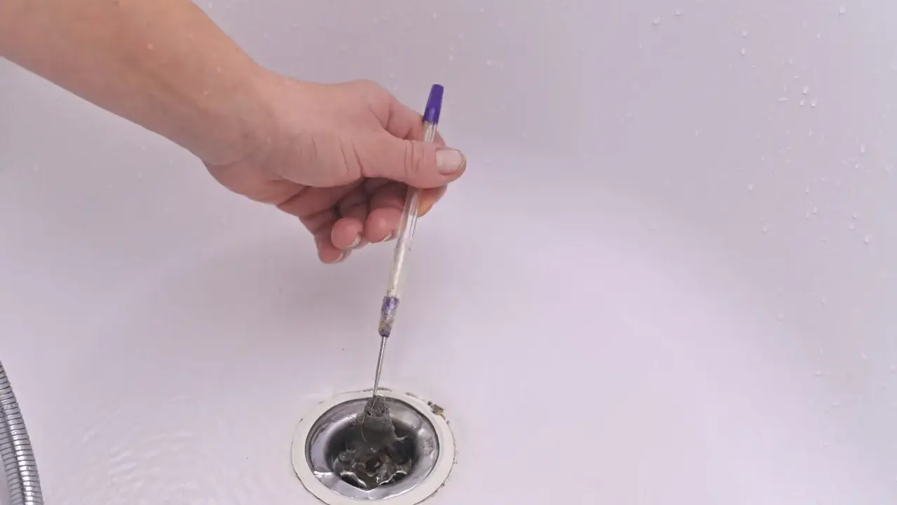 Mano usando un bolígrafo para desatascar desague ducha lleno de pelo.