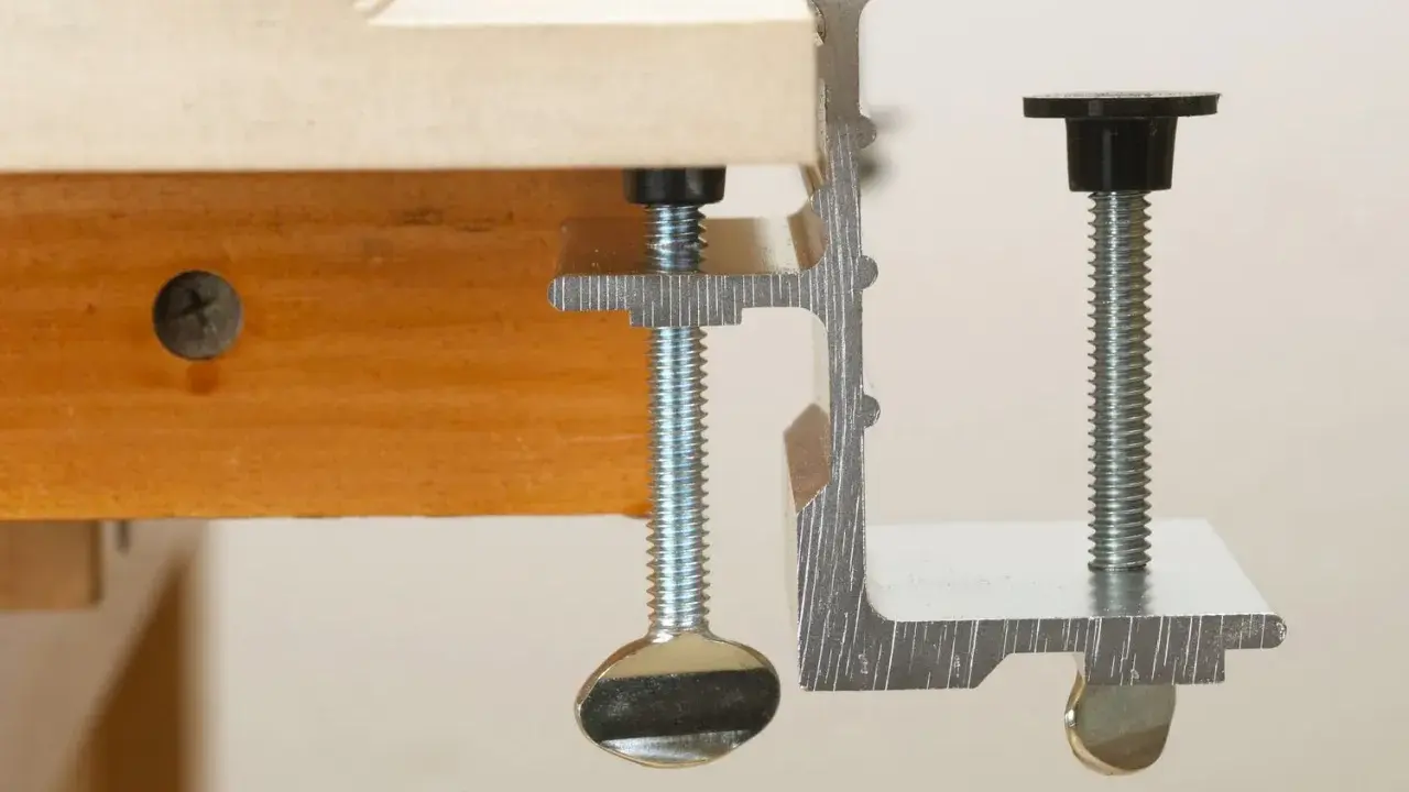 Dos tipos de abrazaderas metálicas sujetan una tabla de madera.