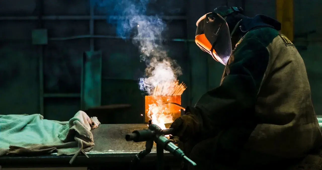 Soldador usa un electrodo rutilo para crear uniones fuertes. El humo y las chispas iluminan la escena industrial.