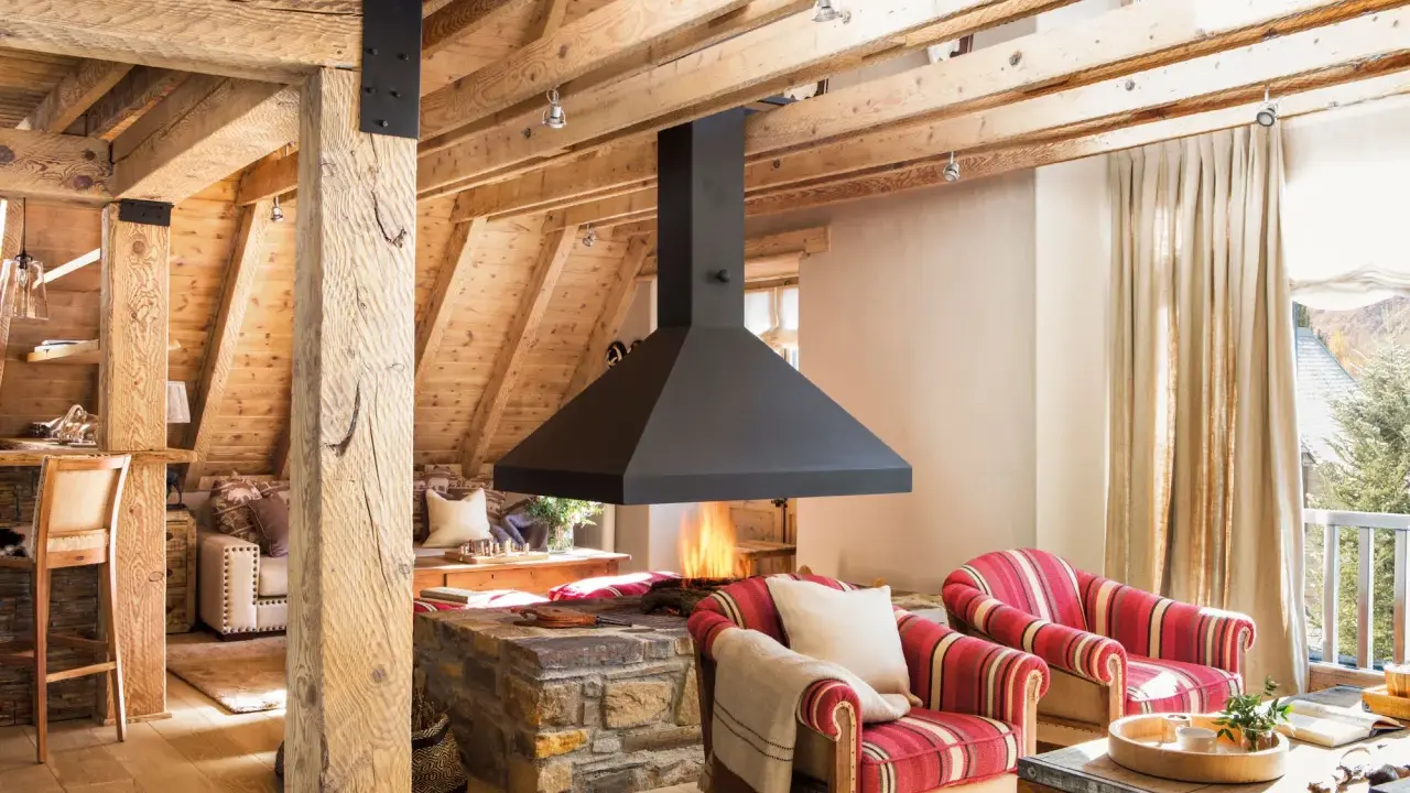 Chimenea central de diseño moderno, uno de los tipos de chimeneas que aporta calidez a este salón rústico con vigas de madera.