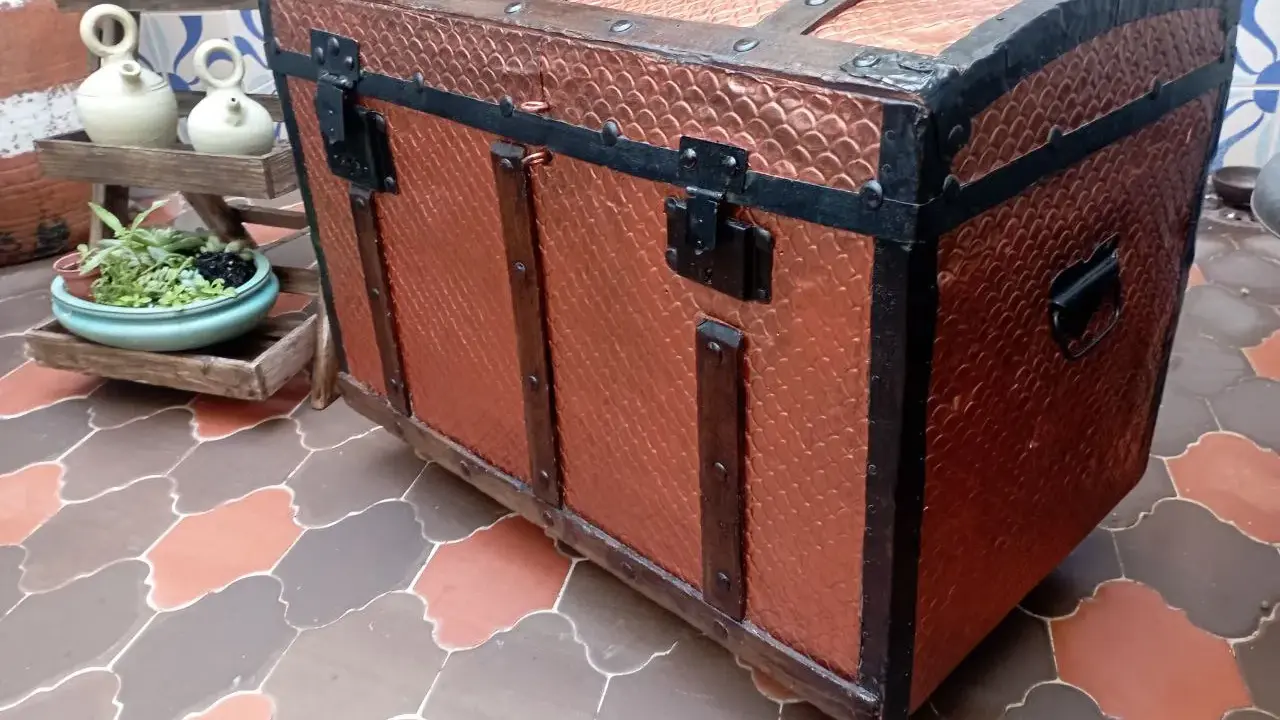 Un baúl antiguo restaurado, con detalles metálicos y acabado en cobre texturizado, listo para guardar tesoros.