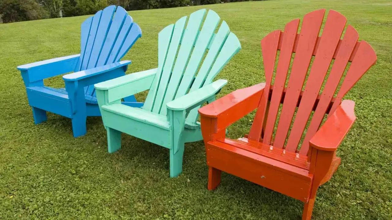 Tres sillas de madera de estilo Adirondack, pintadas de azul, verde menta y naranja, lucen vibrantes sobre el césped. ¡Un proyecto de pintar sillas de madera sin lijar que da vida al jardín!