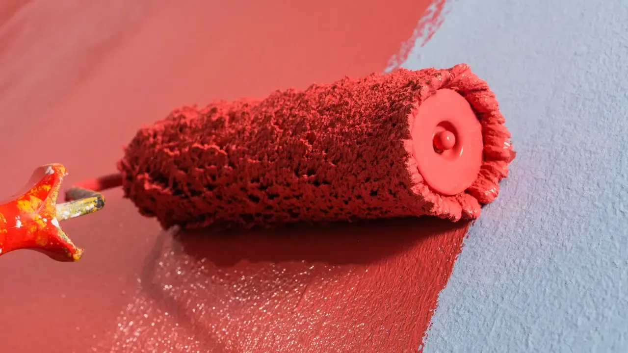 Rodillo de pintura roja creando burbujas al aplicarla sobre pared azul.