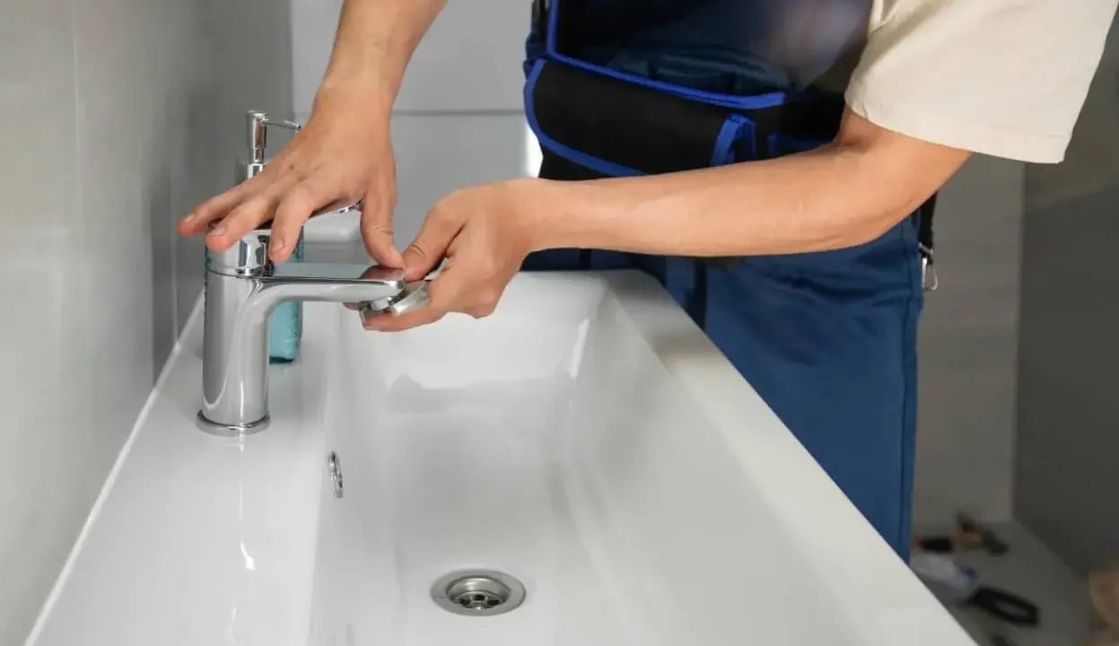 Man con mono azul trabajando en el baño, ajustando un grifo nuevo para cambiar grifo lavabo.