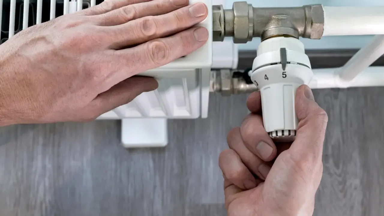 Mano ajusta el termostato de un radiador. El radiador solo calienta la mitad derecha, indicando un posible problema.