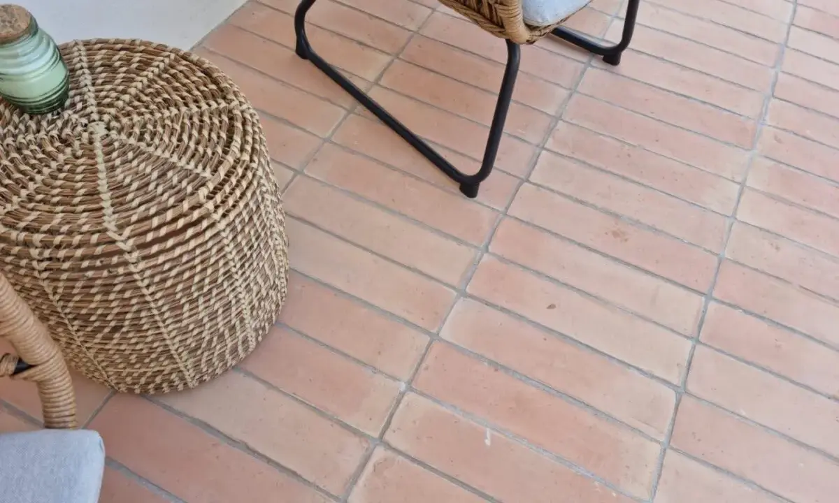 Suelo de baldosas de terracota con juntas limpias, listo para rellenar juntas baldosas suelo. Un cesto de mimbre y una silla de ratán completan la escena.