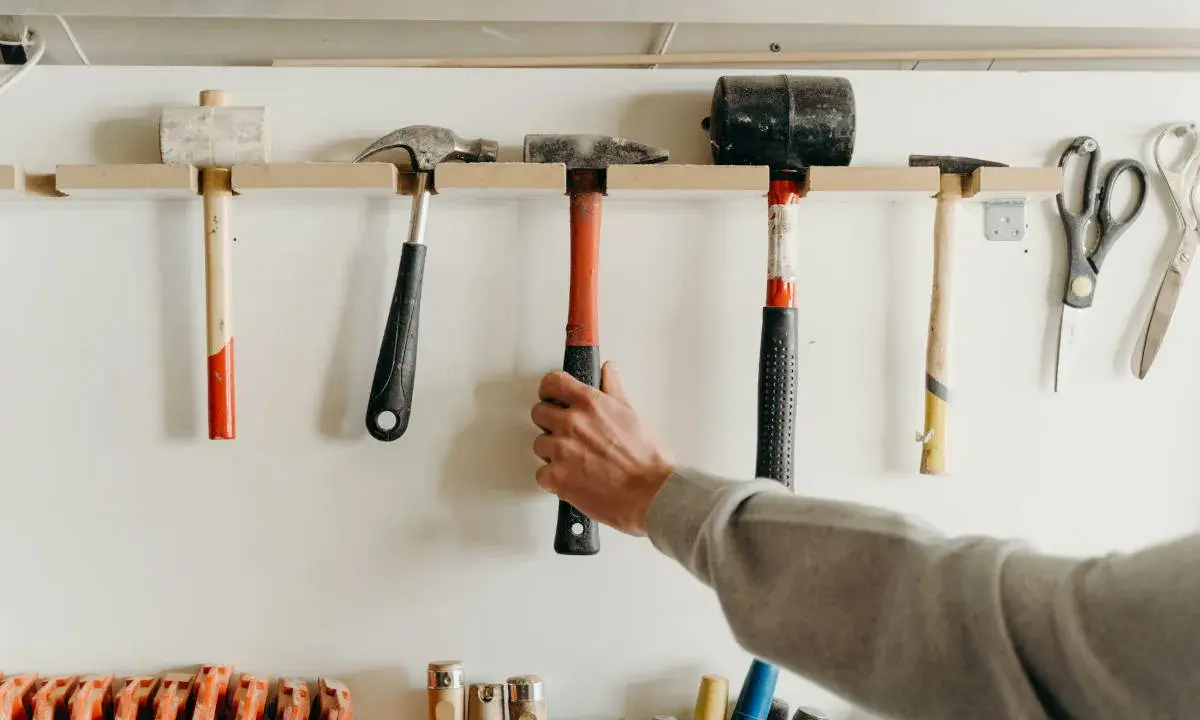 Variedad de tipos de herramientas manuales, incluyendo martillos, mazos y tijeras, colgadas en una pared.