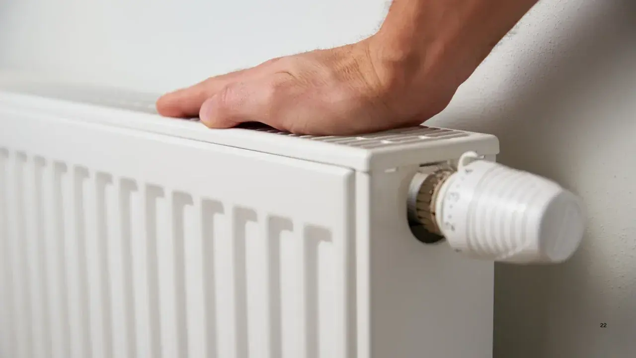 Mano tocando un radiador blanco, listo para cuando encender la calefacción. Termostato visible.