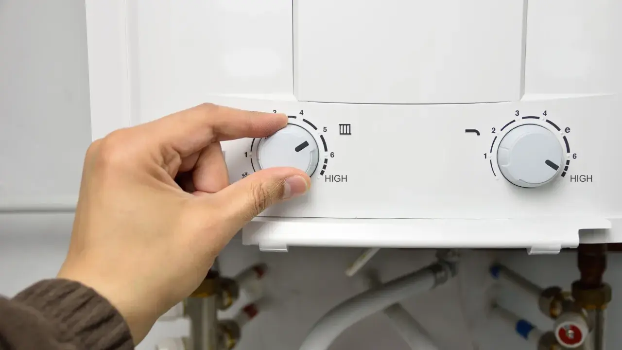 Mano ajustando el dial de temperatura de un termo eléctrico. El agua no sale del termo eléctrico, quizás por la configuración.