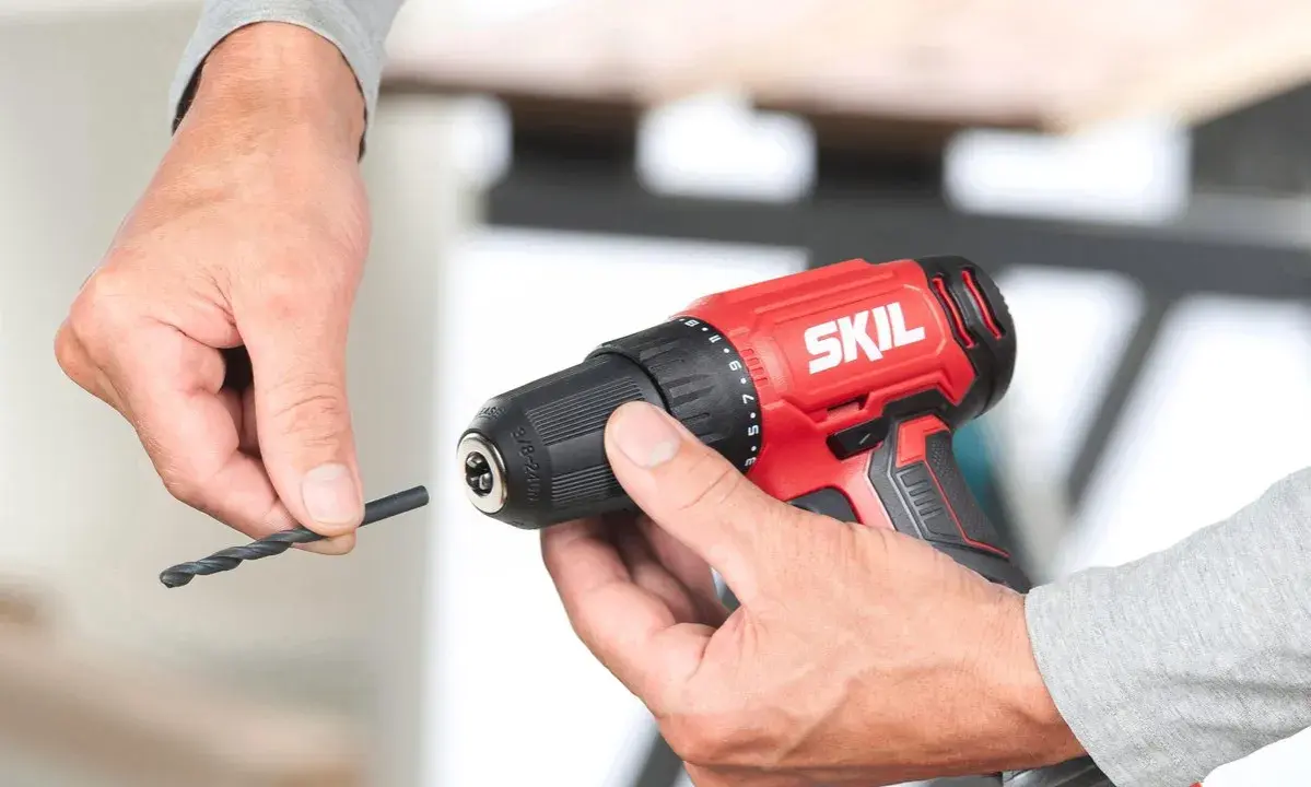 Man insertando una broca en un taladro inalámbrico rojo de la marca SKIL.
