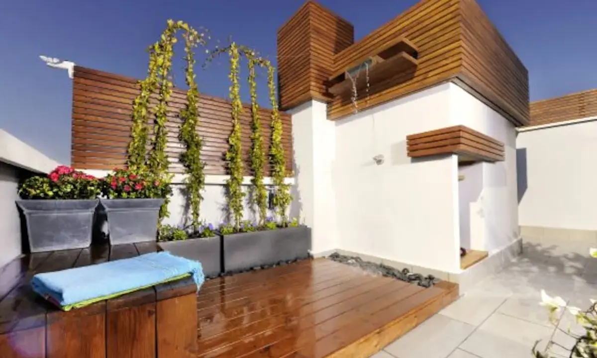 Jardineras de exterior con flores rojas y enredaderas. Un espacio moderno con ducha y terraza de madera.