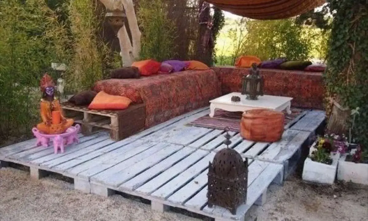 Un rincón zen con sofás y mesas bajas creados con jardineras con palets, cojines coloridos y faroles.