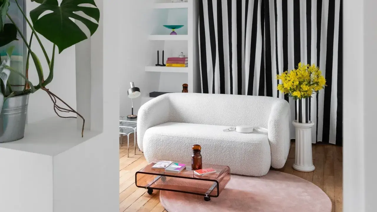 Sofá blanco texturizado, mesa de centro rosa, alfombra redonda y plantas, ideal para una reforma de piso pequeño.