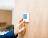Mano ajustando un termostato digital, parte de los sistemas de calefacción, mostrando 20°C en una pared de madera.