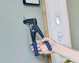 Herramienta para colgar en pladur. Un tornillo se fija a la pared con una remachadora.
