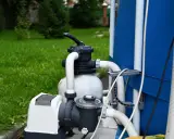 Bomba de agua no arranca solo zumba. El equipo de filtración de piscina, con mangueras blancas y un tanque gris, está junto a una piscina azul.
