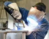 Soldador con máscara y guantes, demostrando cómo soldar con electrodo, creando chispas brillantes.