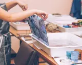Manos sostienen tela con diseño marmoleado sobre una bandeja con agua, lista para la pintura para mármol.