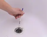 Mano usando un bolígrafo para desatascar desague ducha lleno de pelo.