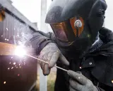 Soldador con casco y guantes usa un electrodo para unir metales, creando chispas brillantes y humo.