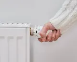 Mano ajustando el termostato de un radiador blanco, pero el radiador no calienta.