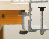 Dos tipos de abrazaderas metálicas sujetan una tabla de madera.