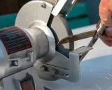 Persona afila tijeras con piedra de esmeril, creando chispas.