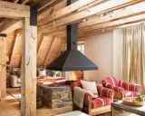 Chimenea central de diseño moderno, uno de los tipos de chimeneas que aporta calidez a este salón rústico con vigas de madera.