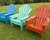 Tres sillas de madera de estilo Adirondack, pintadas de azul, verde menta y naranja, lucen vibrantes sobre el césped. ¡Un proyecto de pintar sillas de madera sin lijar que da vida al jardín!