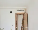 Habitación en obra con rejilla de preinstalación aire acondicionado en la pared, puerta abierta y escalera.