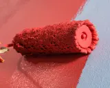 Rodillo de pintura roja creando burbujas al aplicarla sobre pared azul.