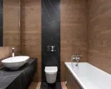 Baño moderno con lavabo ovalado, bañera y un inodoro con salida vertical o horizontal, todo rodeado de azulejos de madera y mármol negro.