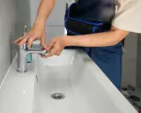 Man con mono azul trabajando en el baño, ajustando un grifo nuevo para cambiar grifo lavabo.