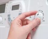 Mano ajustando el dial de una caldera de gas para cambiar la temperatura.