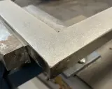 Un ángulo metálico en una escuadra de carpintero, listo para ser pulido con herramientas de acabado.
