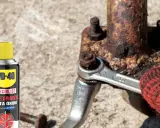 WD-40 ayuda a sacar tornillo roto de pieza oxidada. Llave inglesa y guante rojo en acción.