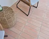 Suelo de baldosas de terracota con juntas limpias, listo para rellenar juntas baldosas suelo. Un cesto de mimbre y una silla de ratán completan la escena.