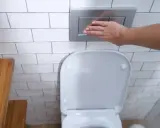 Mano presionando el botón de descarga de una cisterna empotrada, un ejemplo de los modernos tipos de cisternas wc.