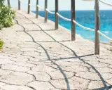 Camino de piedra con barandilla y mar azul. Un ejemplo de cómo hacer hormigón impreso para exteriores.