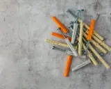 Una tabla de tacos y tornillos de diferentes colores (naranja, gris y beige) sobre una superficie de cemento.