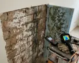 Herramientas para diagnosticar y como aislar una pared de la humedad: medidor de humedad, cámara térmica y guantes sobre ladrillos afectados por moho.