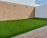 Un patio con césped artificial verde vibrante, paredes de piedra y madera. Ideal para aprender como colocar césped artificial.