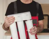 Técnico con mono rojo y gris, sosteniendo un sistema de ósmosis inversa para cambiar filtros.