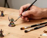 Mano pintando miniaturas con diferentes tipos de pinceles. Se aprecian pinceles para detalles y generales.