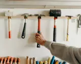 Variedad de tipos de herramientas manuales, incluyendo martillos, mazos y tijeras, colgadas en una pared.